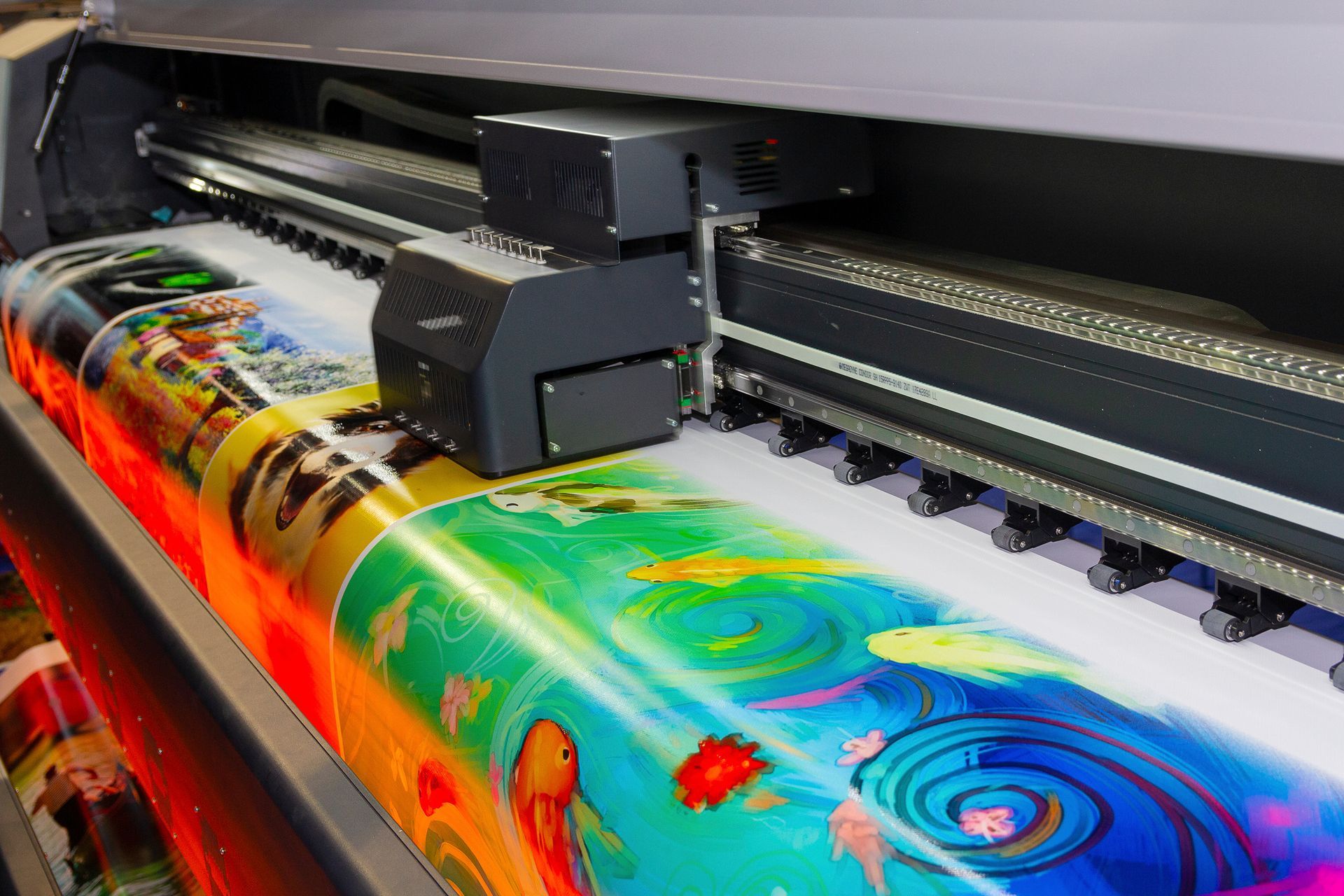 A close-up of a large format printing machine in operation, printing a colourful digital print