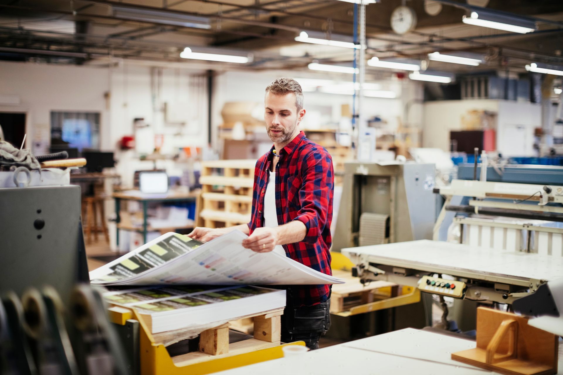 A man working in a printing press office holding and checking a large set of digital prints
