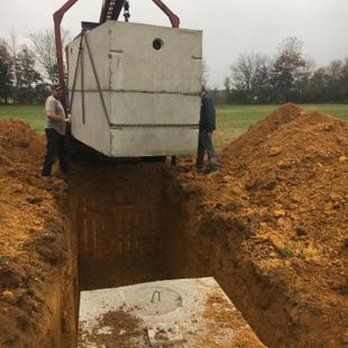 A man is lifting a septic tank into a hole in the ground.