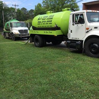 Two septic tank trucks are parked next to each other in a grassy field.