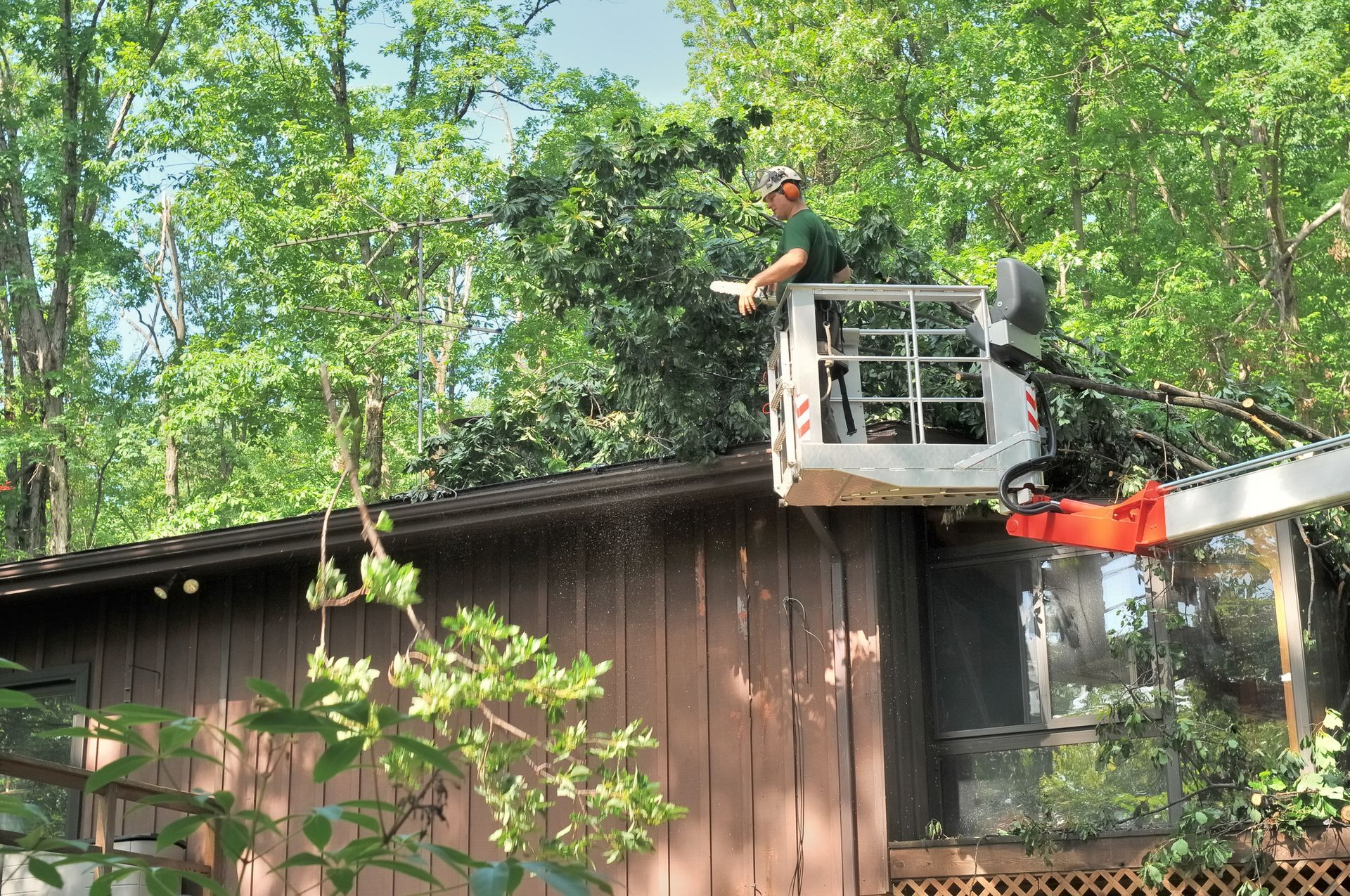 Tree trimming service using lift to remove branches near house roof in wooded area.