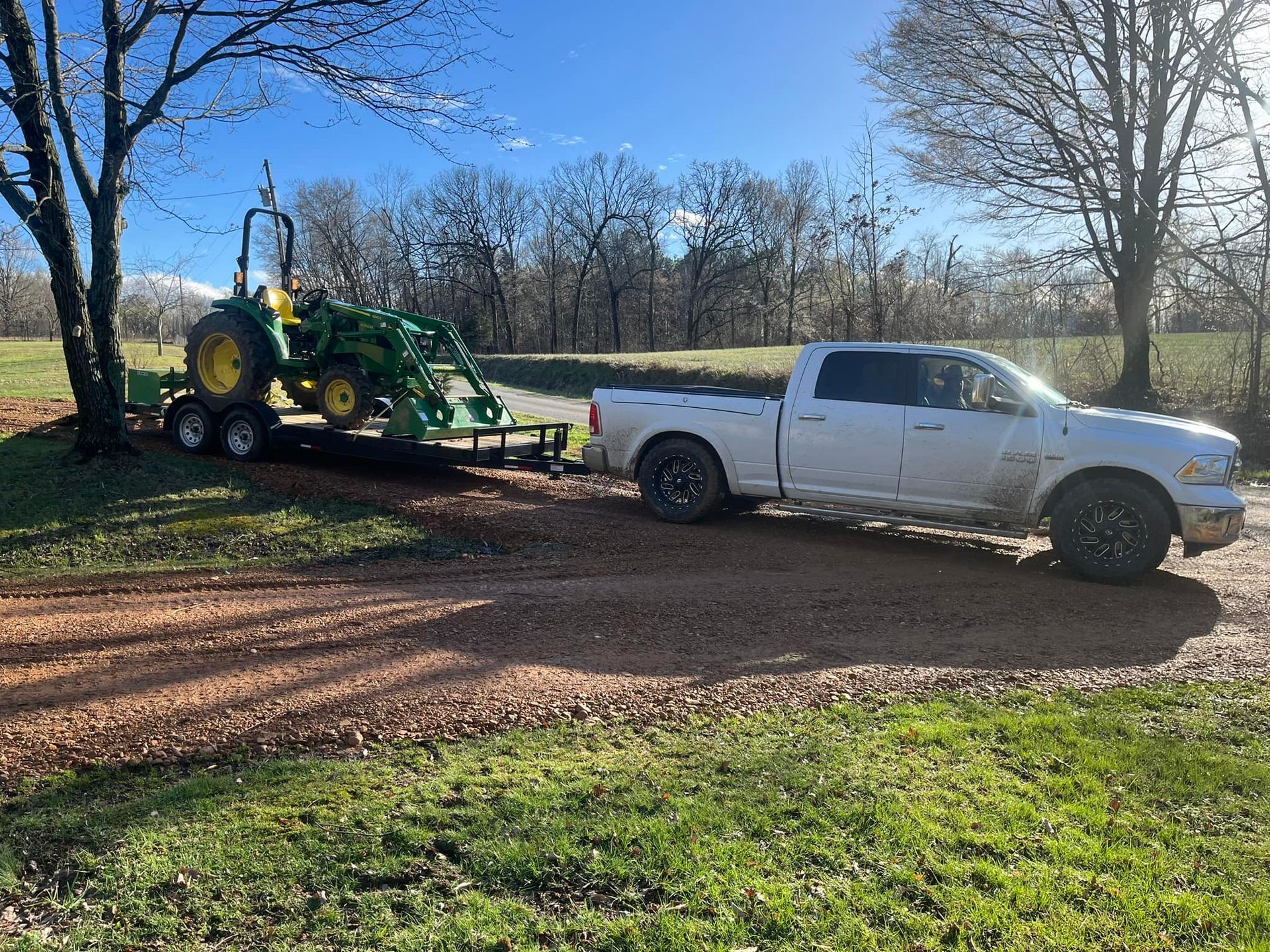 A white truck is towing a green tractor on a trailer.