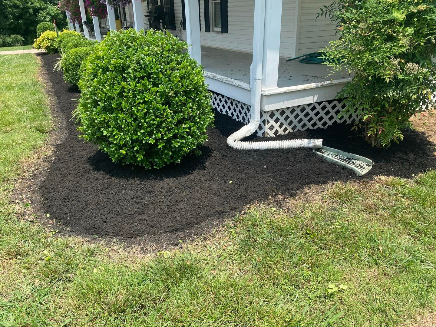 A house with a porch and a sprinkler in front of it.