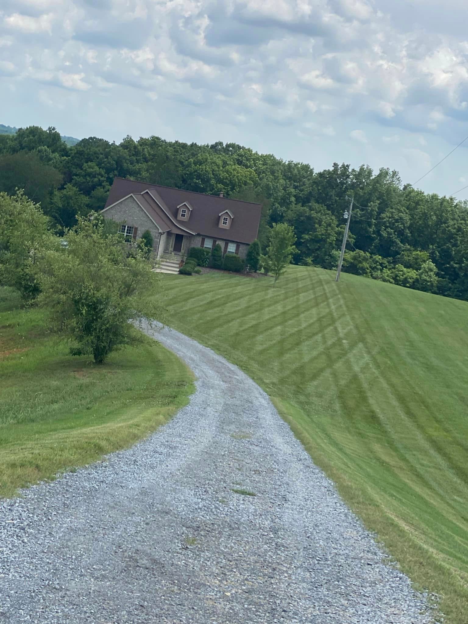 A gravel road leading to a house on top of a grassy hill.