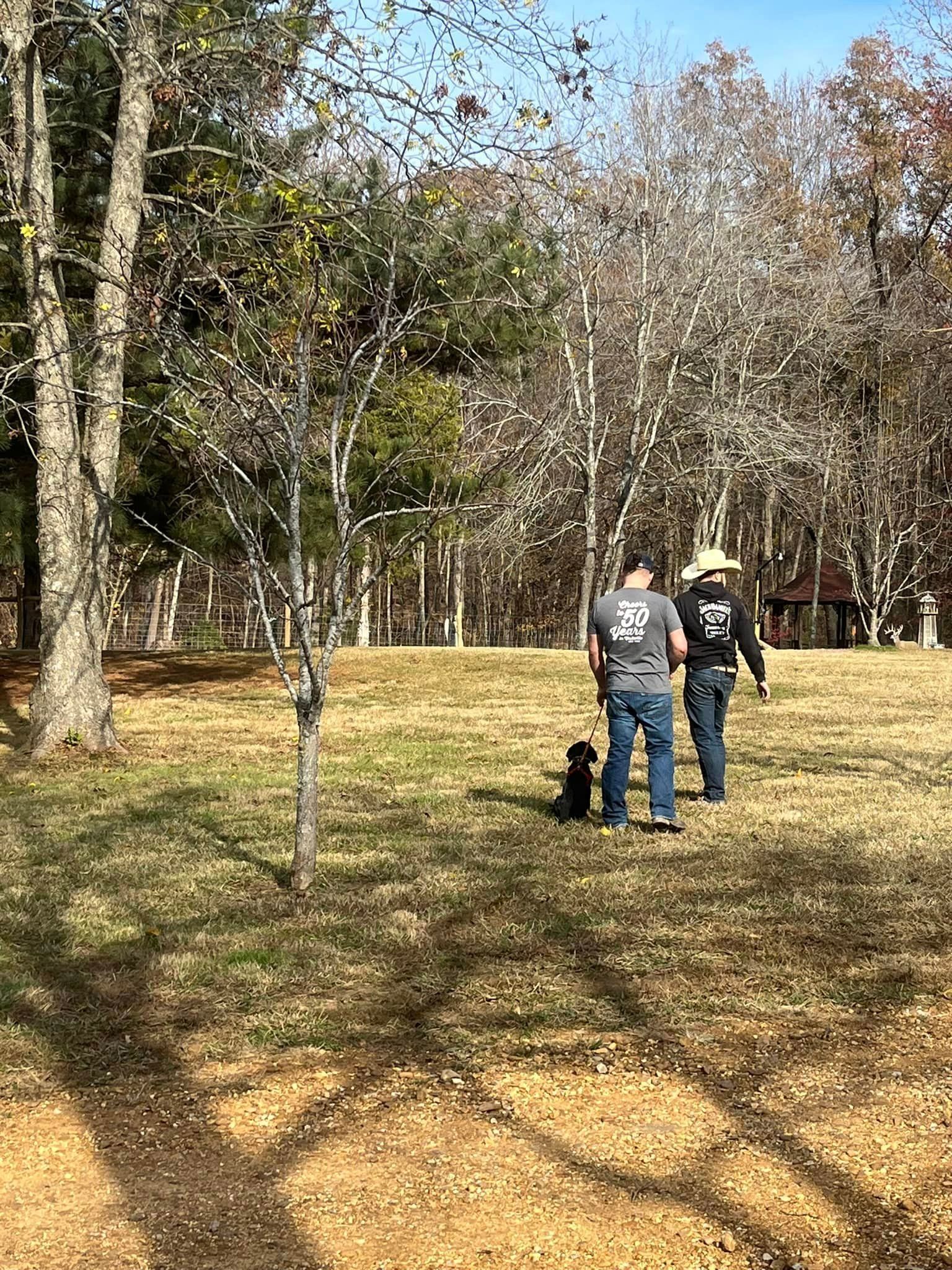 A man and a woman are walking a dog in a field.