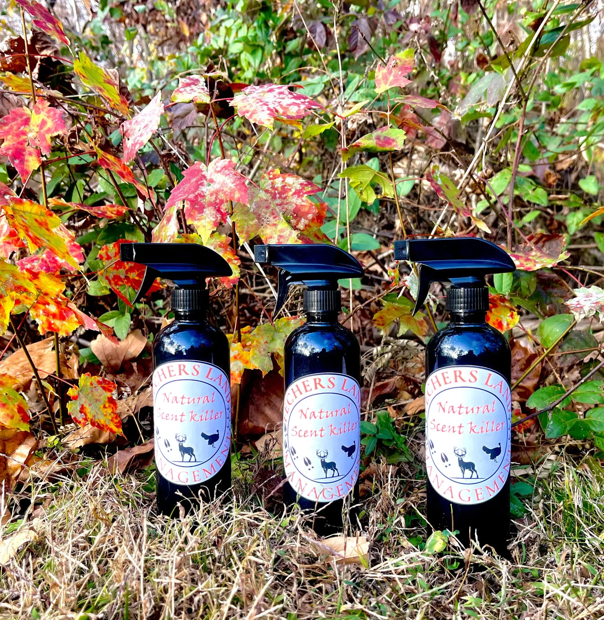Three spray bottles are sitting in the grass in front of a bush.