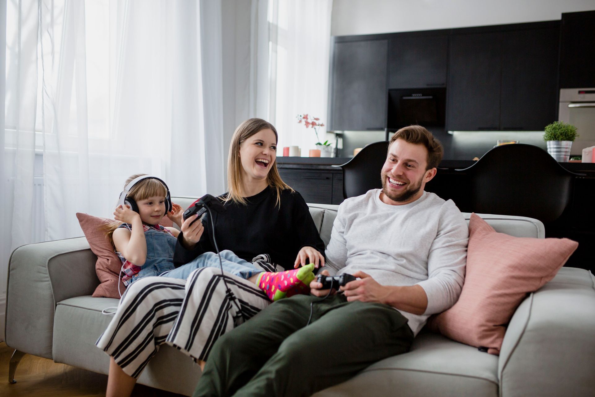 Family of three laughing while playing video games on a couch.