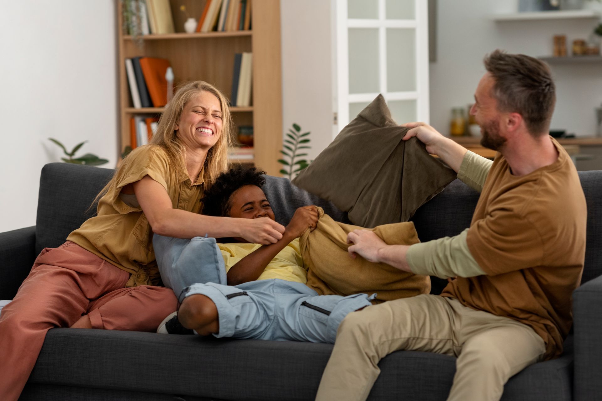 Family of three laughing and playing with pillows on a couch.