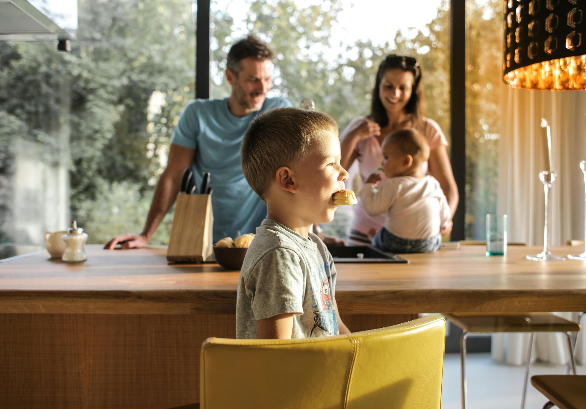 Family in modern kitchen; boy eating, parents in background.