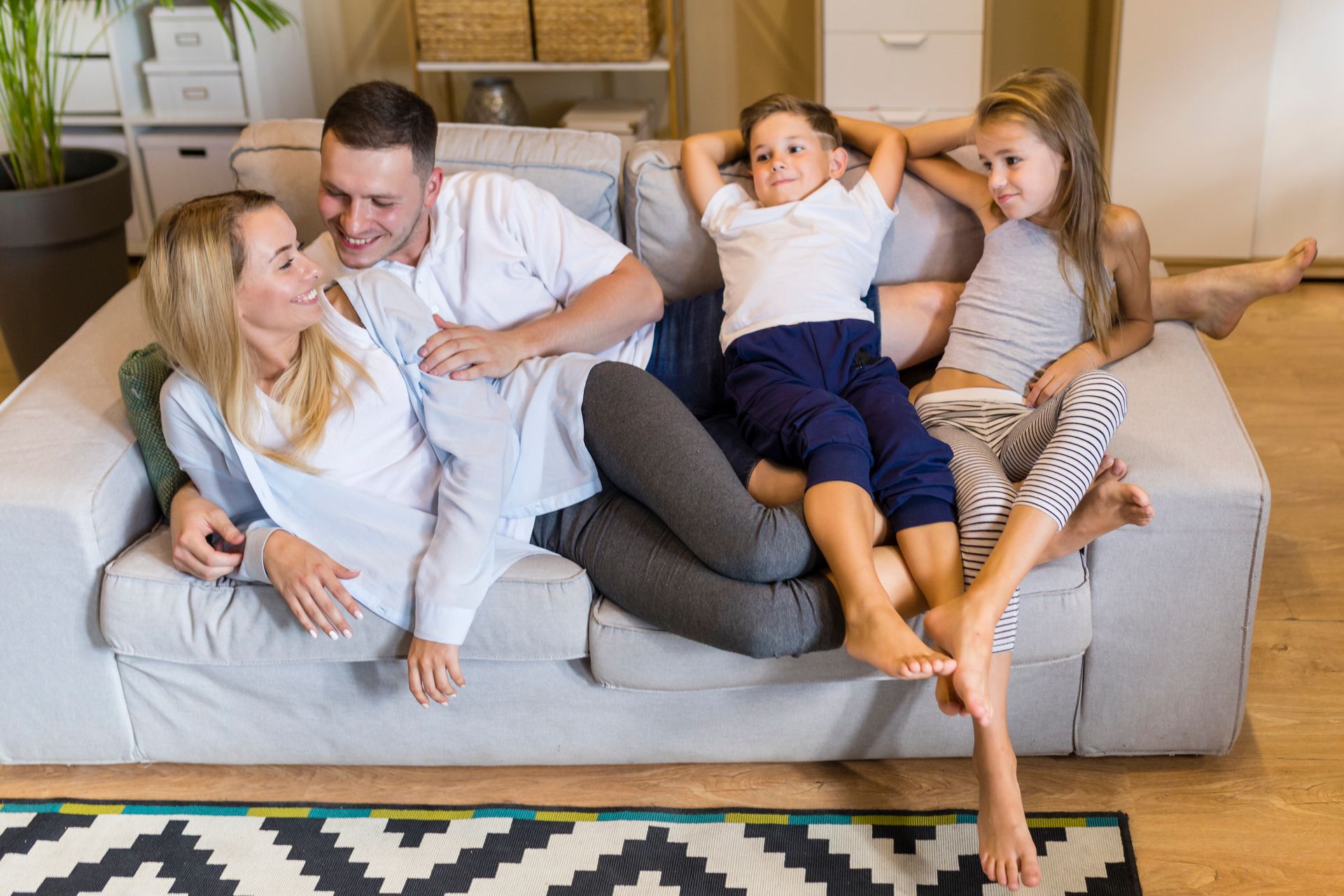 Family of four relaxing on a couch, smiling at each other.