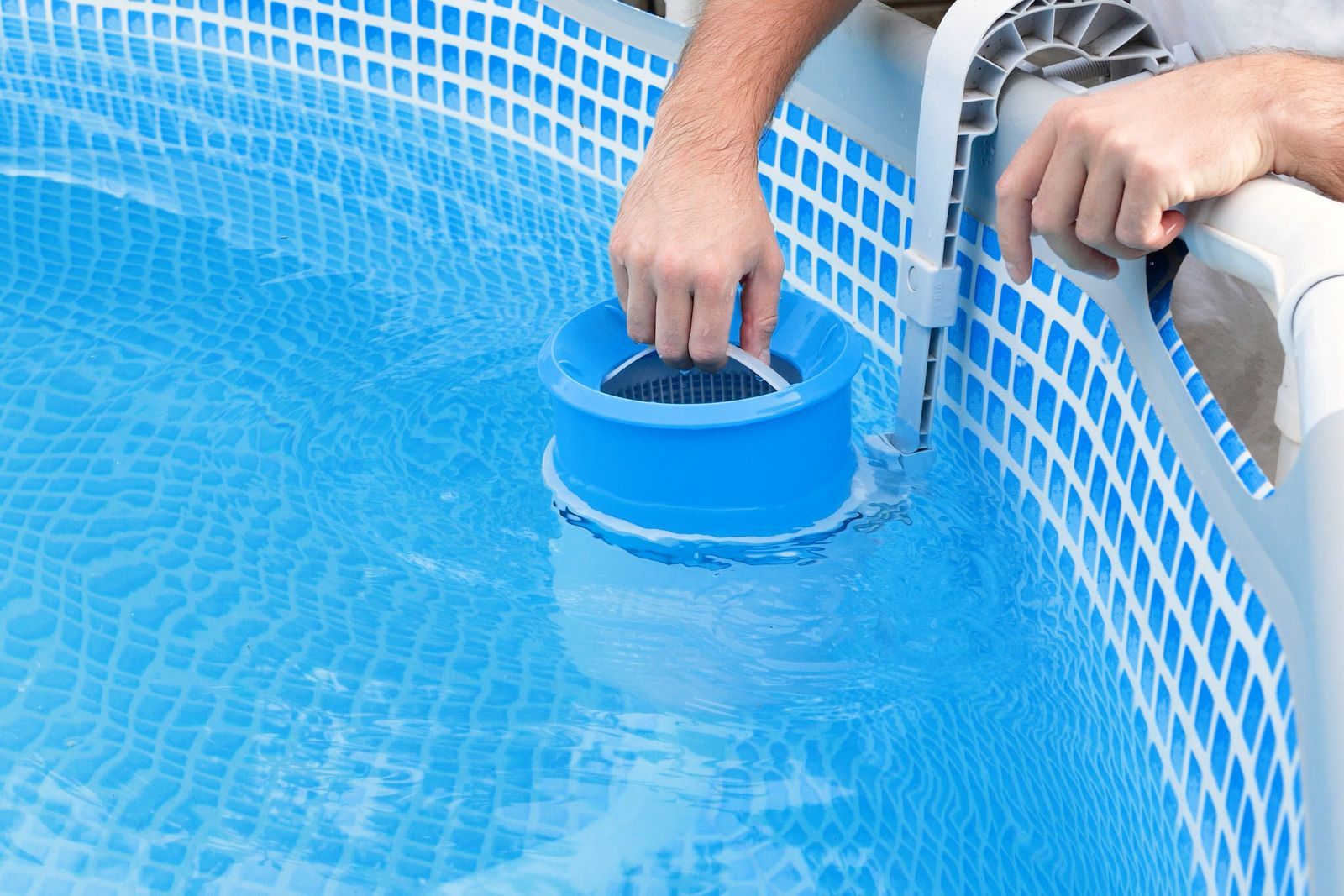 Person cleaning a blue pool with a skimmer; close up.