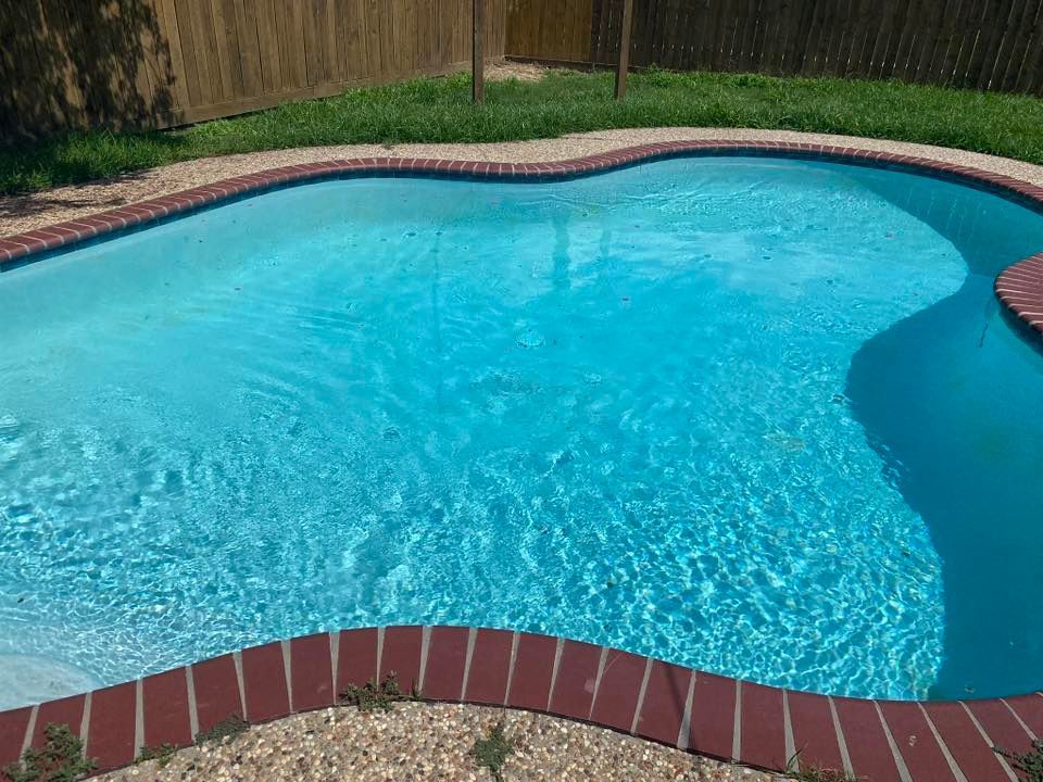 A large swimming pool with a brick border and a fence in the background.