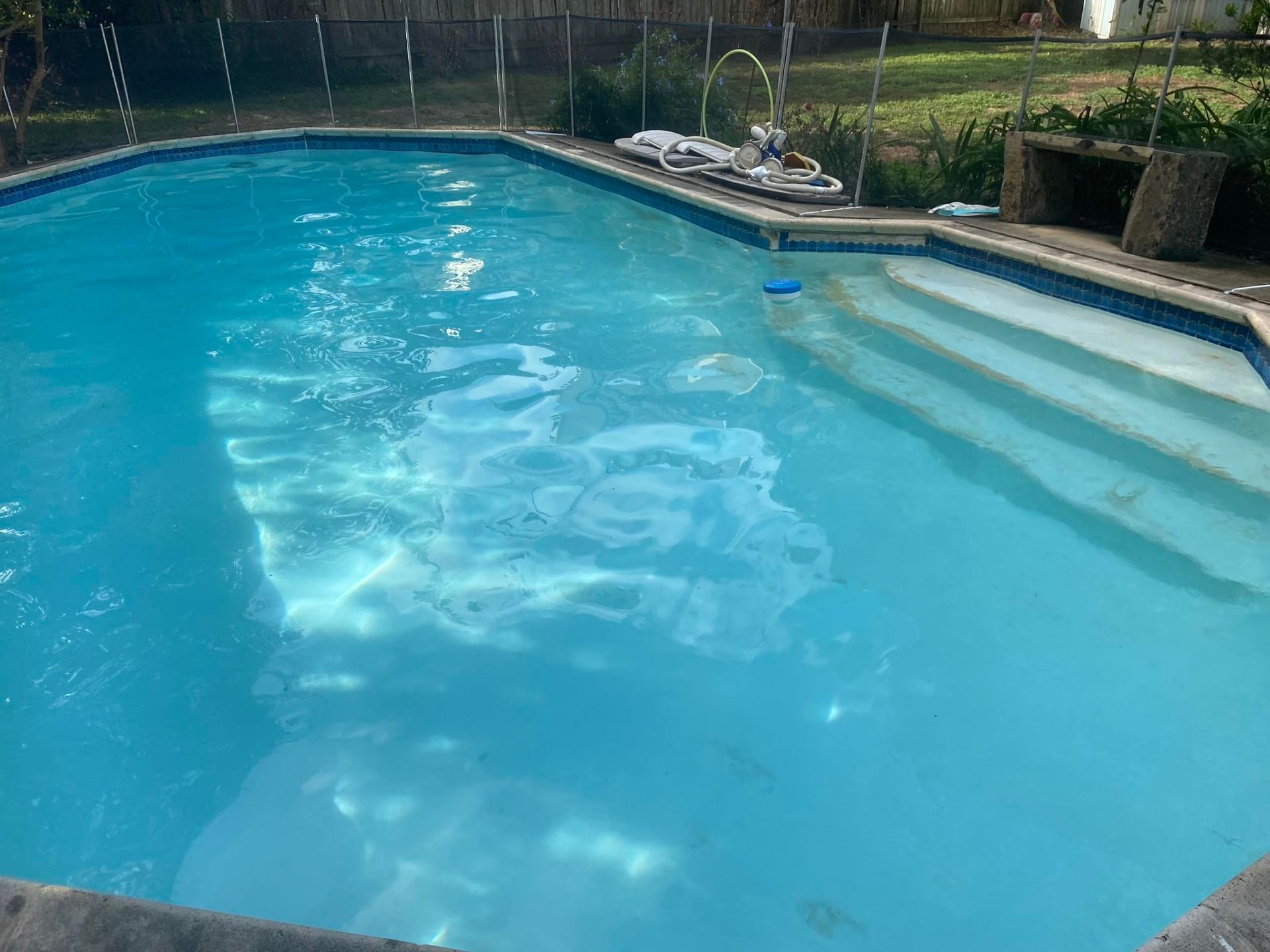 A large swimming pool with blue water and stairs in a backyard.