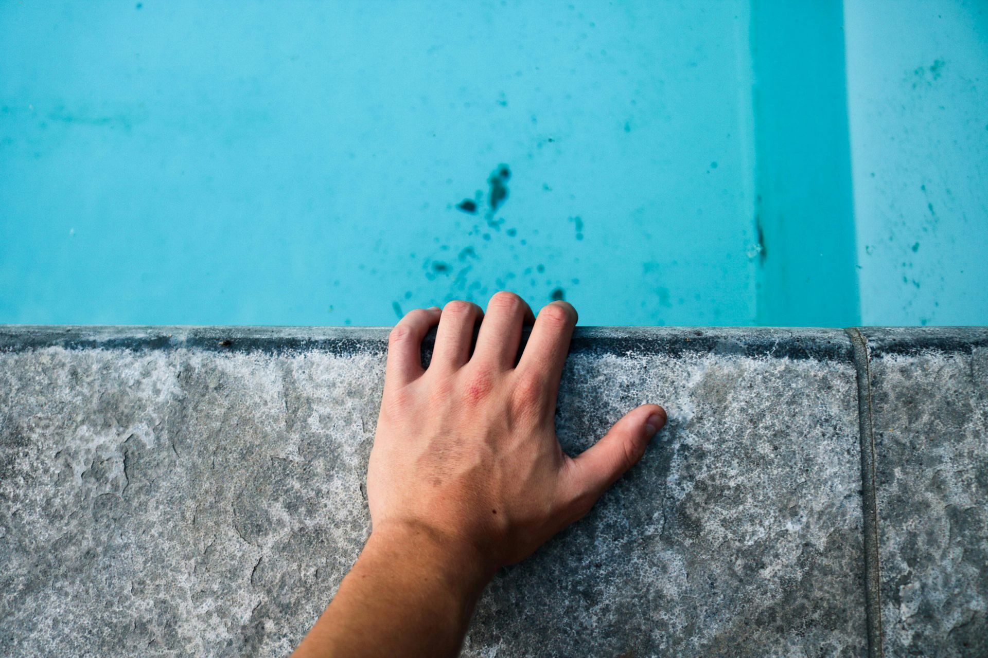 A person 's hand is reaching for the edge of a swimming pool.
