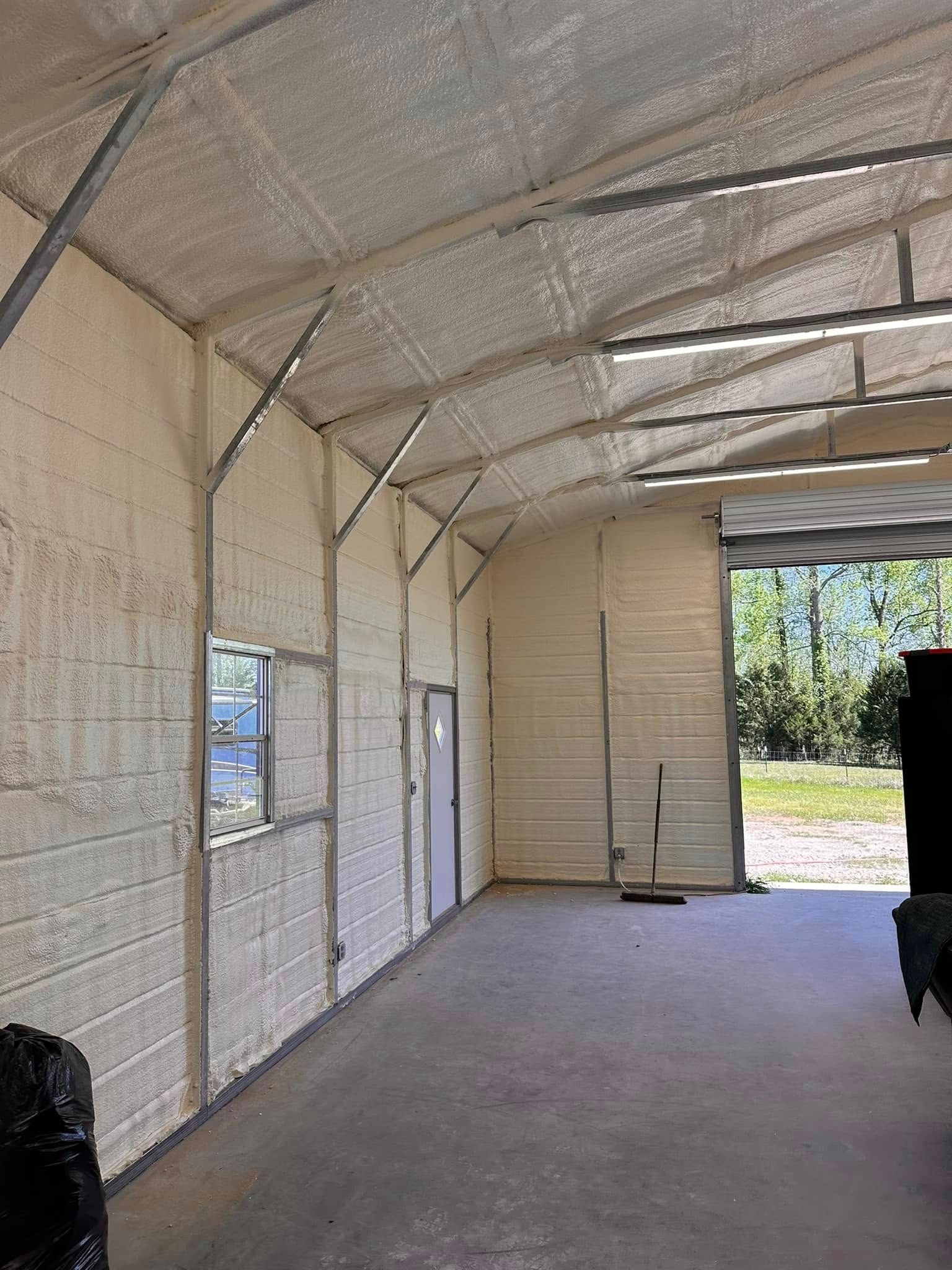 Empty metal-roofed garage with concrete floor, windows, and an open door to a sunny yard