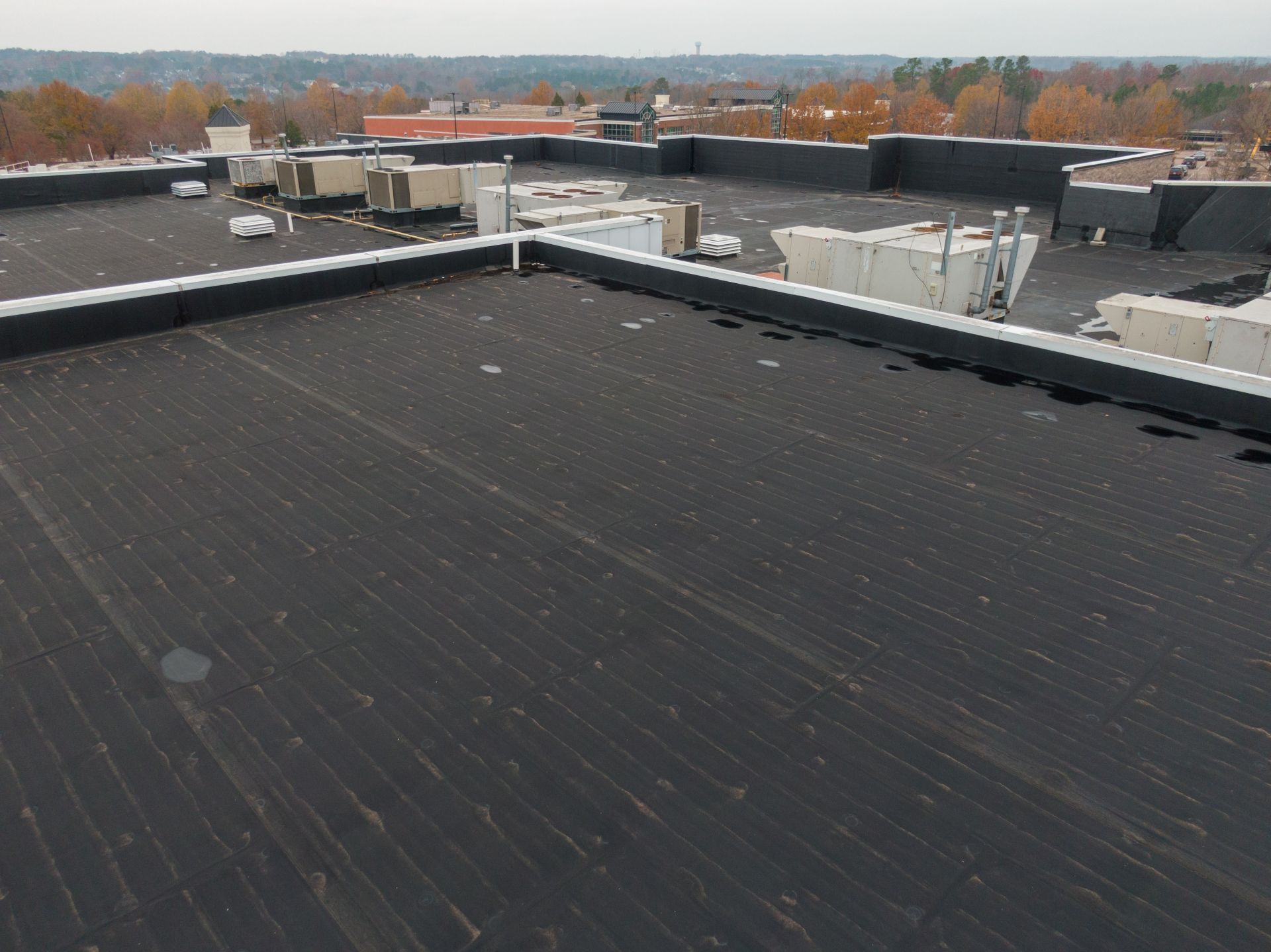 Flat black rooftop with HVAC units and autumn trees in the distance