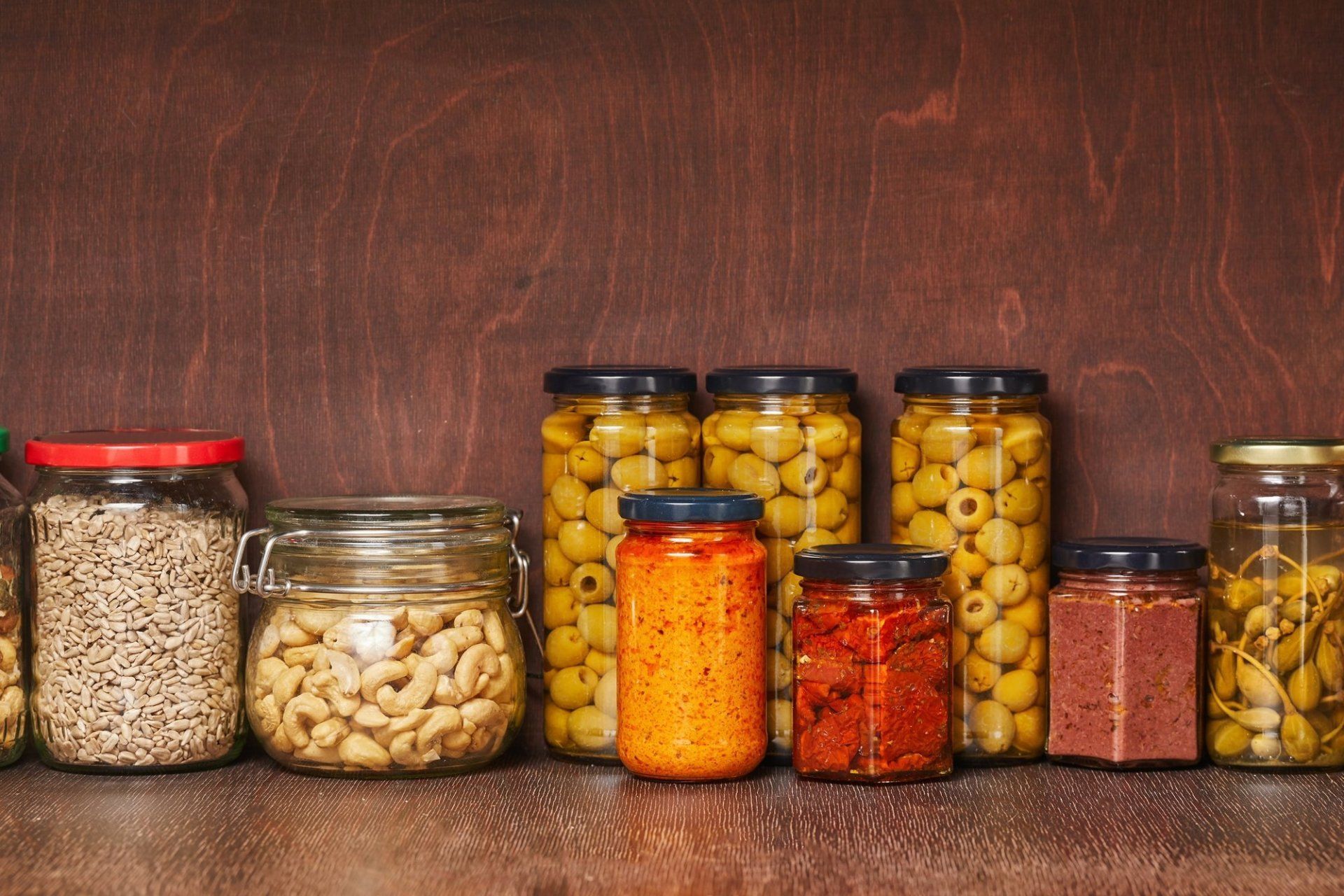 pantry shelf with jars of various foods including olives, cashews and seeds