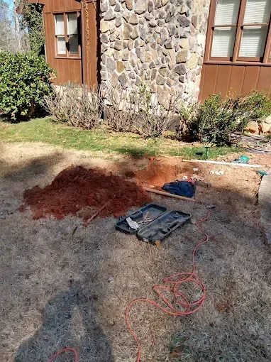 Exterior scene: Tools and red fibers near a stone-walled building with brown trim and windows, on a grassy area.