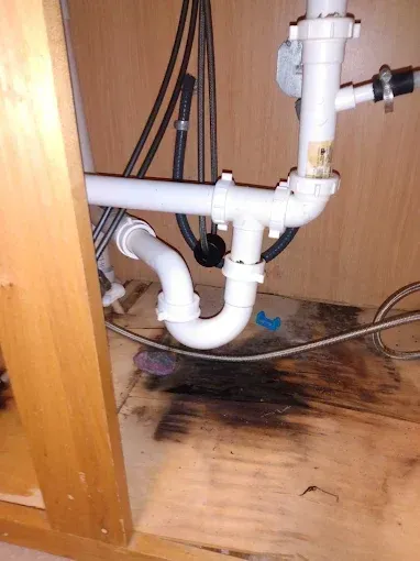 Under-sink plumbing with a curved pipe and potential water damage on the cabinet floor.