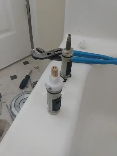 Two faucet cartridges on a bathtub edge with tools; bathroom setting.