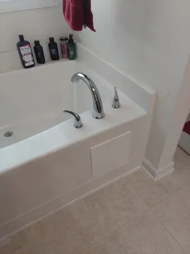 White bathtub with chrome fixtures, water running; toiletries on ledge, red towel.