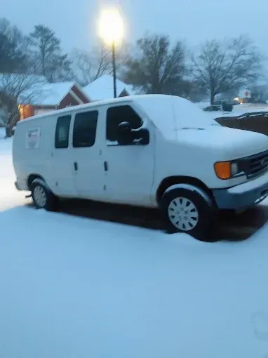 White van covered in snow parked on a snow-covered street with a street light in the background.