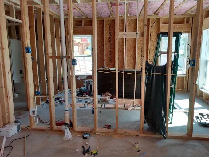 Interior framing of a building under construction, showing wooden studs, plumbing, and electrical boxes.