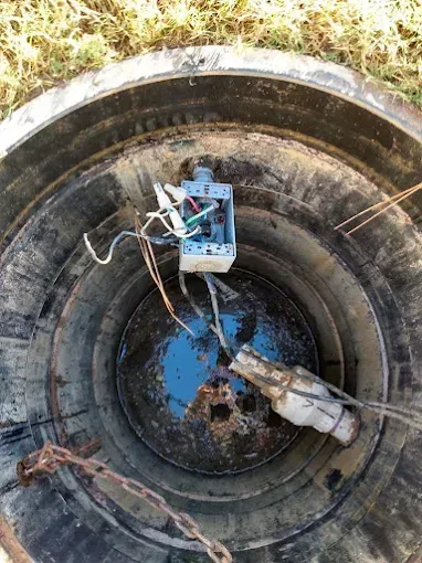 Open electrical junction box and wires inside a dark, concrete well.