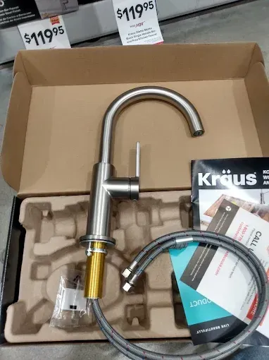 Silver kitchen faucet in a box, with price tag, hose, and instructions.