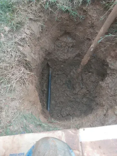 Hole dug in the ground, with a pipe visible. A shovel rests in the hole.
