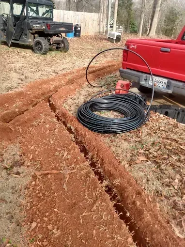 Trenches dug in red earth with black tubing and a red truck, likely for an irrigation system.