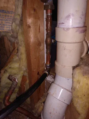 Plumbing pipes: copper and black water lines joined to white PVC pipes in a wall cavity, with insulation.
