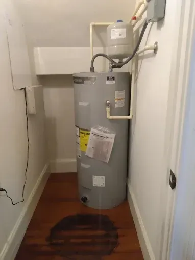 A water heater in a narrow closet with water damage on the floor.