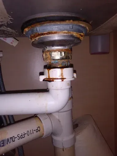 Close-up of a corroded sink drain assembly with rust and drips. 