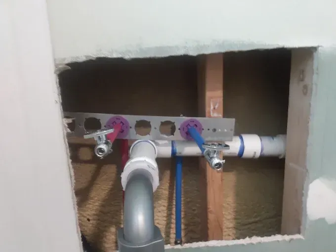 Plumbing pipes with shut-off valves and mounting bracket in wall opening. 