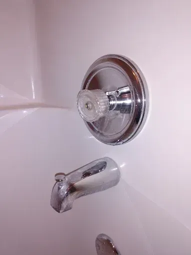 Chrome faucet and tub spout on a white bathtub, with a clear handle and circular trim.