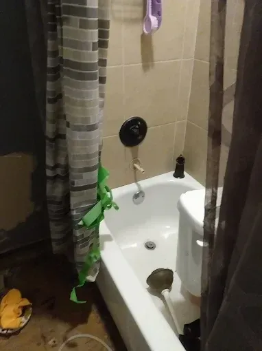 A small white bathtub with a shower head, shower curtain, and a nearby toilet.