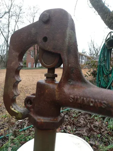 Rusty, vintage Simmons water pump outdoors with a handle and lever.