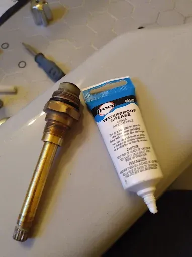 Faucet valve next to a tube of waterproof grease on a white surface.