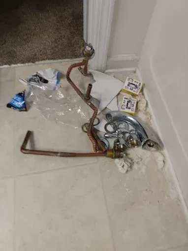 Plumbing fixtures and copper pipes on bathroom floor next to a white wall.