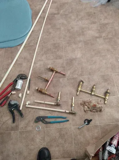 Plumbing tools and pipes laid on a tiled floor. Includes wrenches, valves, and PVC pipes.