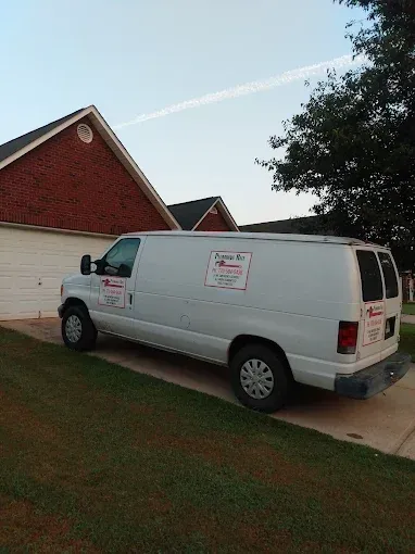 White service van parked on residential lawn, next to a brick house and garage.