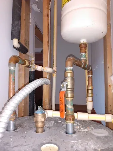 Plumbing system with water heater, pipes, and expansion tank in a wall cavity.