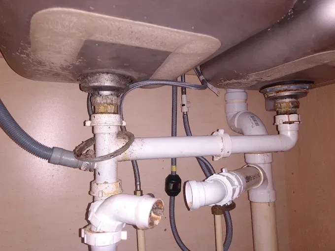 Undersink plumbing with white pipes, a dishwasher drain hose, and two stainless steel sinks.