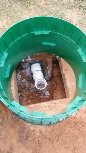 Green plastic septic tank lid open, revealing PVC piping in a square hole.