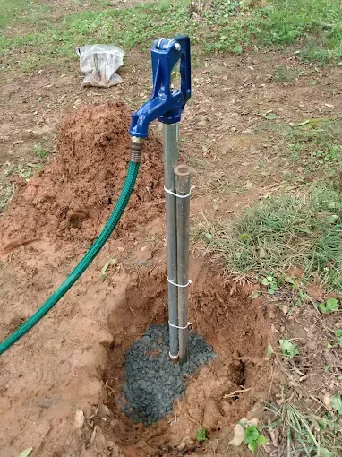 Blue water pump installed in a hole in the ground with a connected green hose.