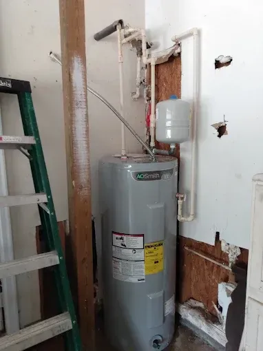 Water heater in a damaged corner, with a ladder and pipes visible.