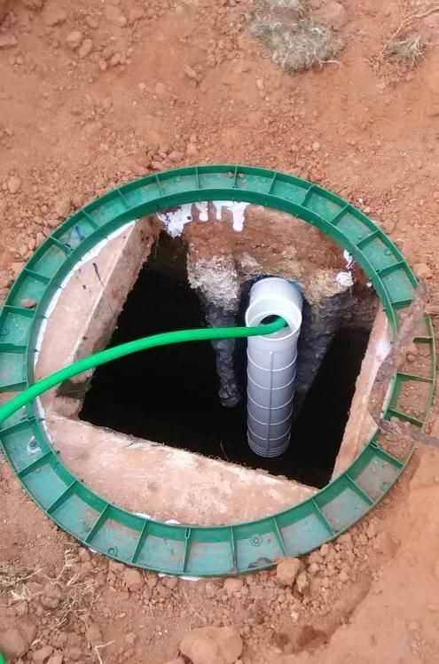 Open septic tank with a green hose and cylindrical filter.