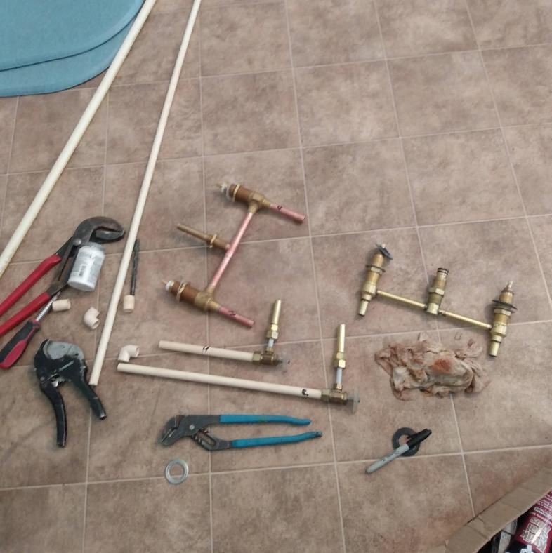 Plumbing tools and copper pipes on a tiled floor.