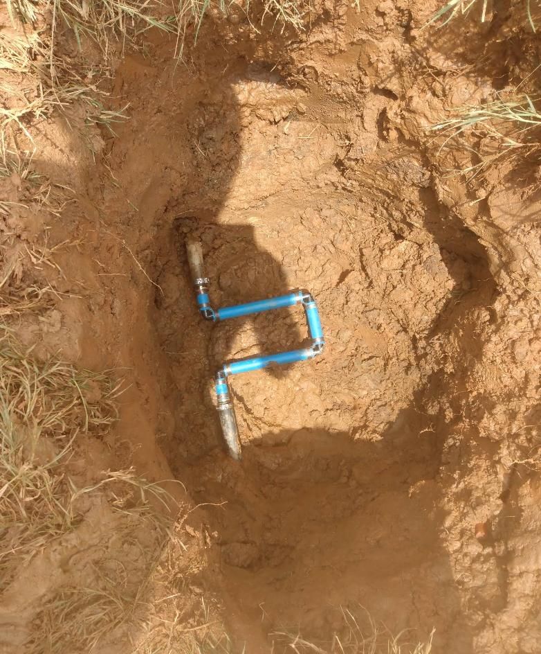 Blue irrigation pipe fittings buried in a dirt hole.